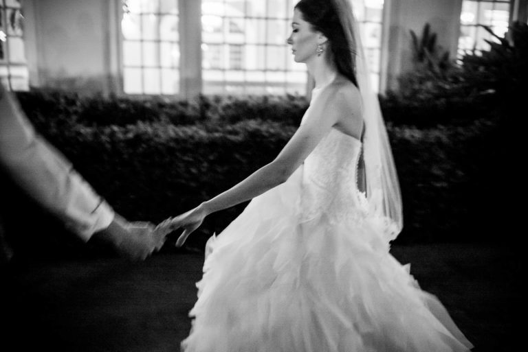 Bride and groom hold hands walking along pathway at an evening wedding reception hotel-galvez-wedding-philip-thomas-photography-028