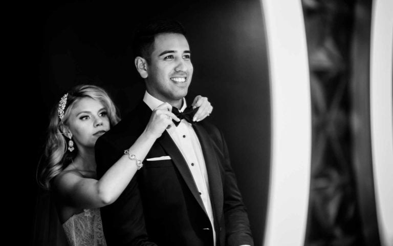 Married couple shows bride fixes grooms tie in restroom at St. Anthony's historic hotel moments before a wedding reception. Photography by Texas wedding photographer Philip Thomas