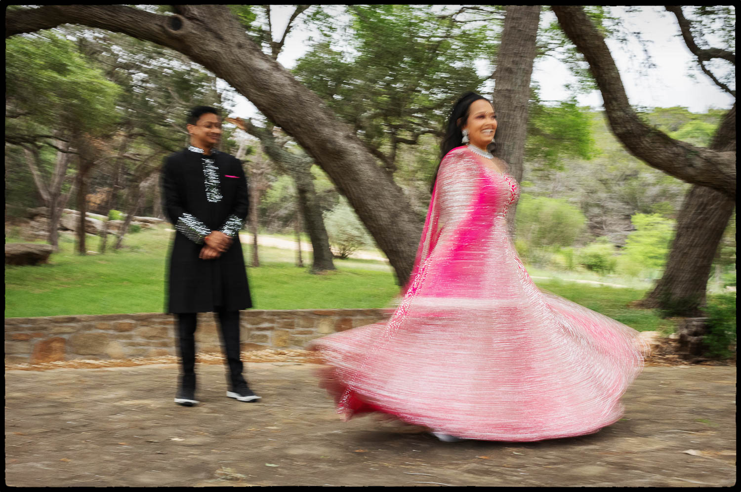 a woman in a pink dress and a man in a black suit shows motion as she swirls her dress