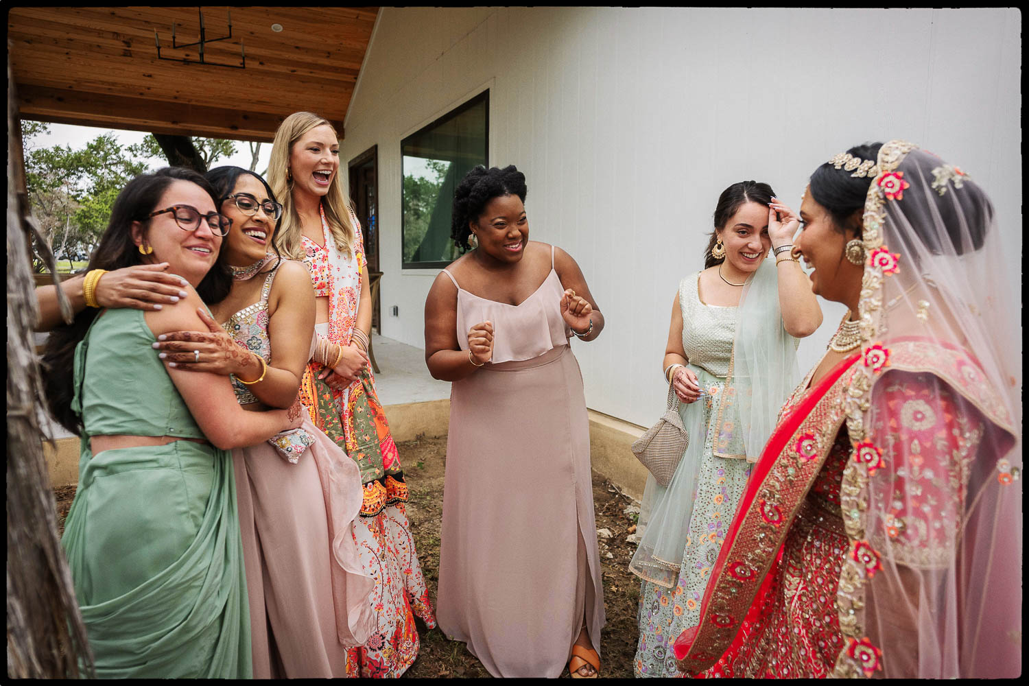 a group of women in dresses hugs the bride at first look