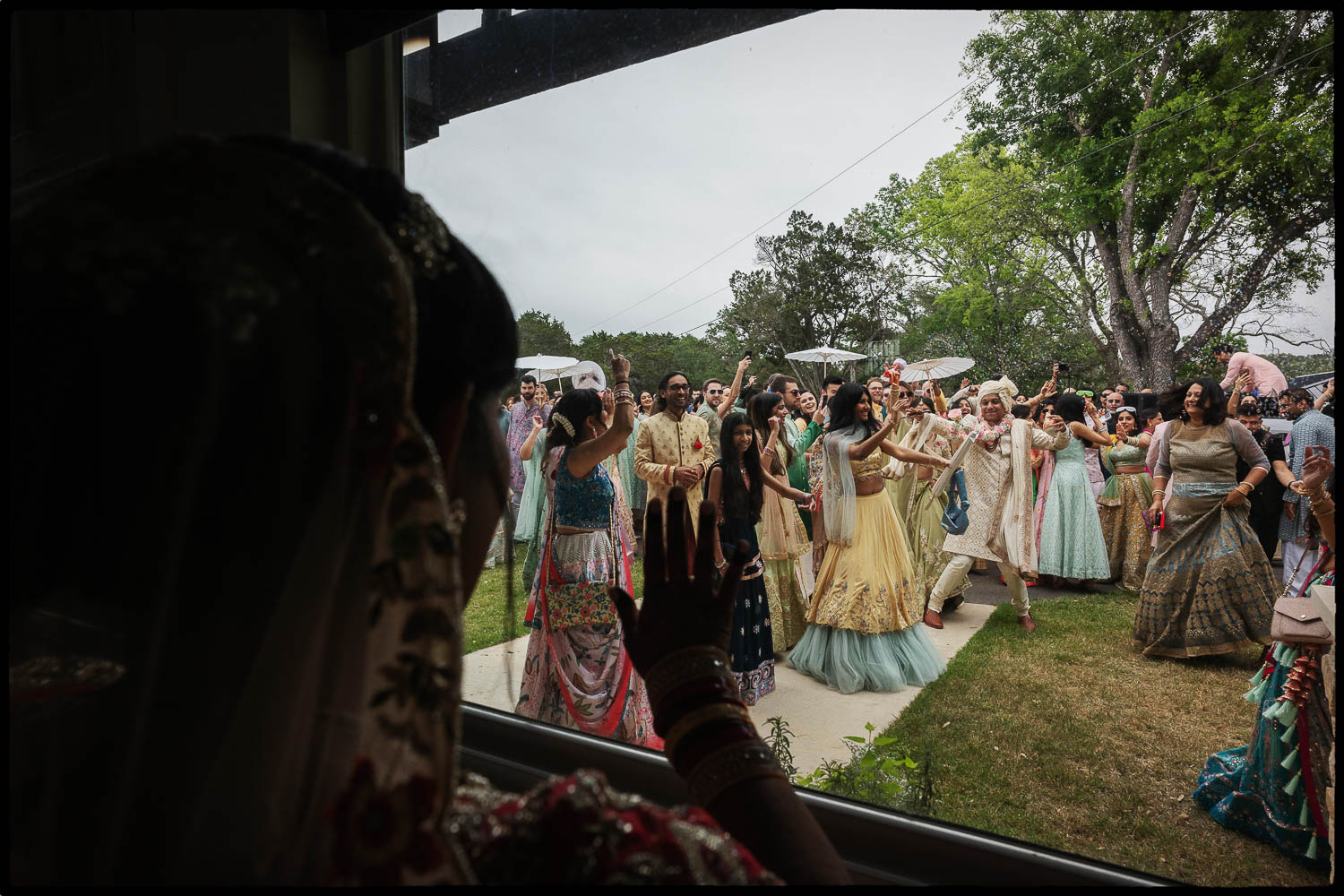 a group of people in traditional clothing  celebrating during the baraat shows the bride observing through the window